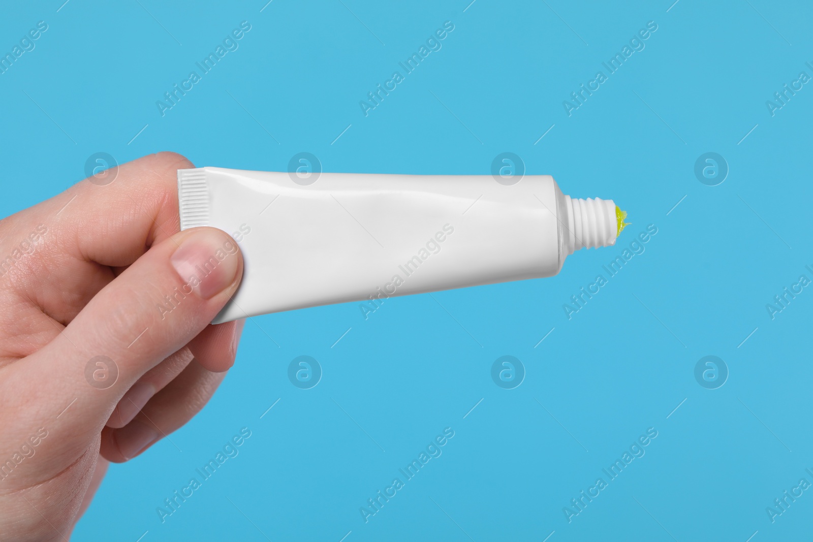 Photo of Man holding tube of ointment on light blue background, closeup