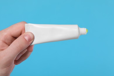 Man holding tube of ointment on light blue background, closeup