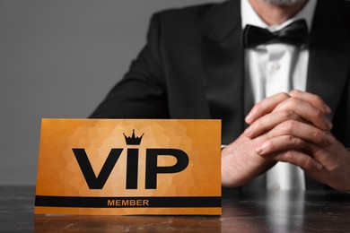 Man sitting at table with VIP sign on grey background, closeup