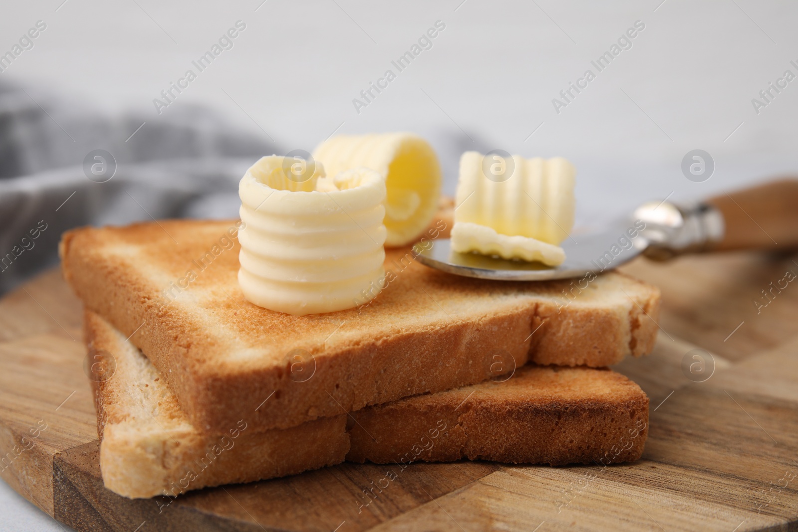 Photo of Tasty butter curls, knife and toasts on wooden board, closeup