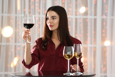 Beautiful young woman tasting luxury wine at table indoors