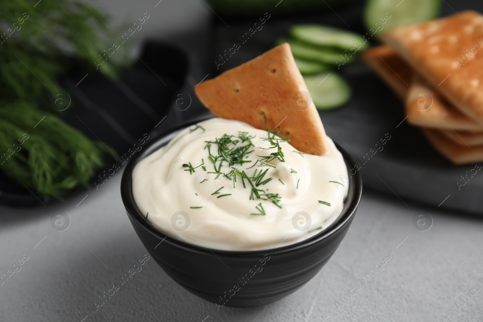 Photo of Tasty creamy dill sauce with cracker in bowl on grey table, closeup