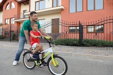 Happy father teaching his son to ride bicycle on street
