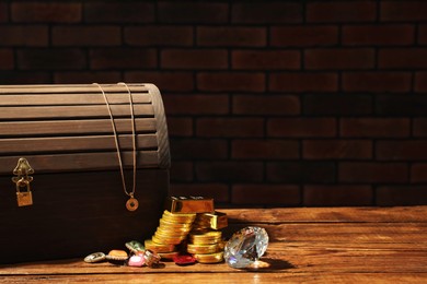 Photo of Treasure chest, gold bars, coins, jewelry and gemstones on wooden table. Space for text