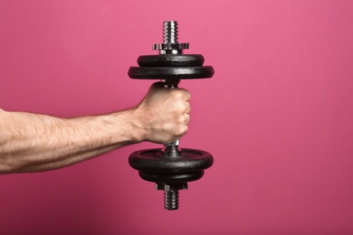 Photo of Male athlete holding metal dumbbell on color background. Space for text