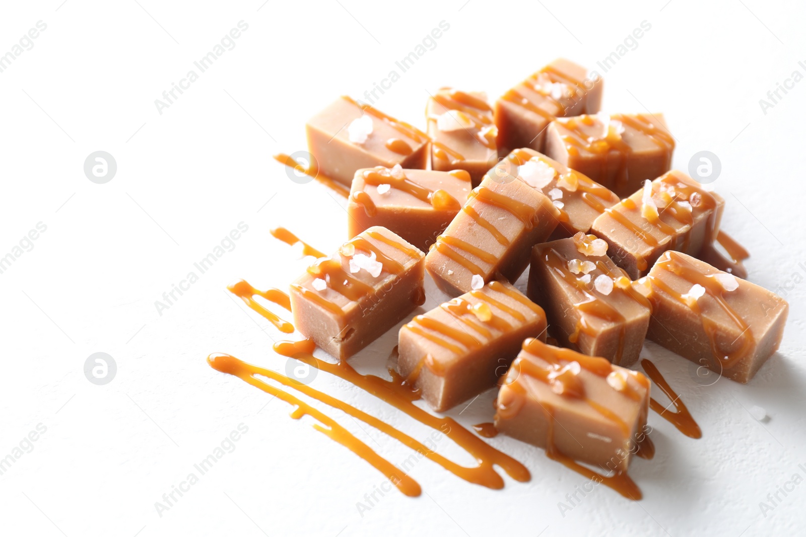 Photo of Tasty candies, caramel sauce and salt on white table, space for text