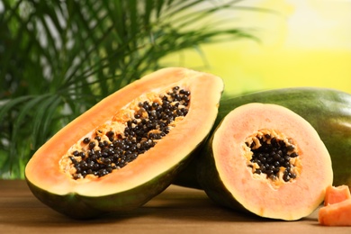 Photo of Fresh juicy cut papayas on wooden table against blurred background, space for text