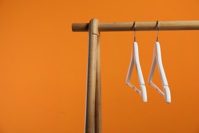 Photo of Empty clothes hangers on wooden rack against orange background. Space for text