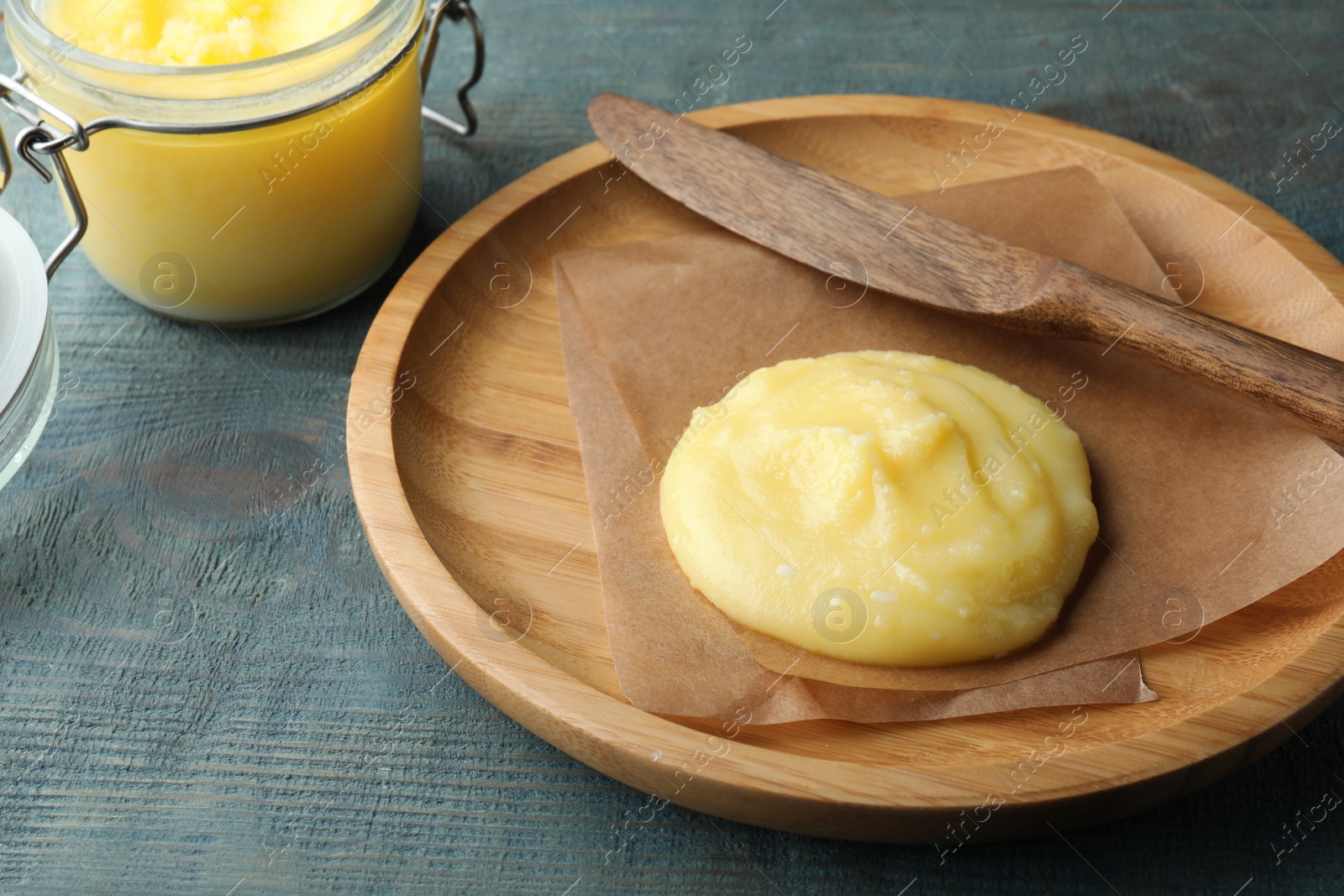 Photo of Plate and knife with Ghee butter on light blue wooden table, closeup.