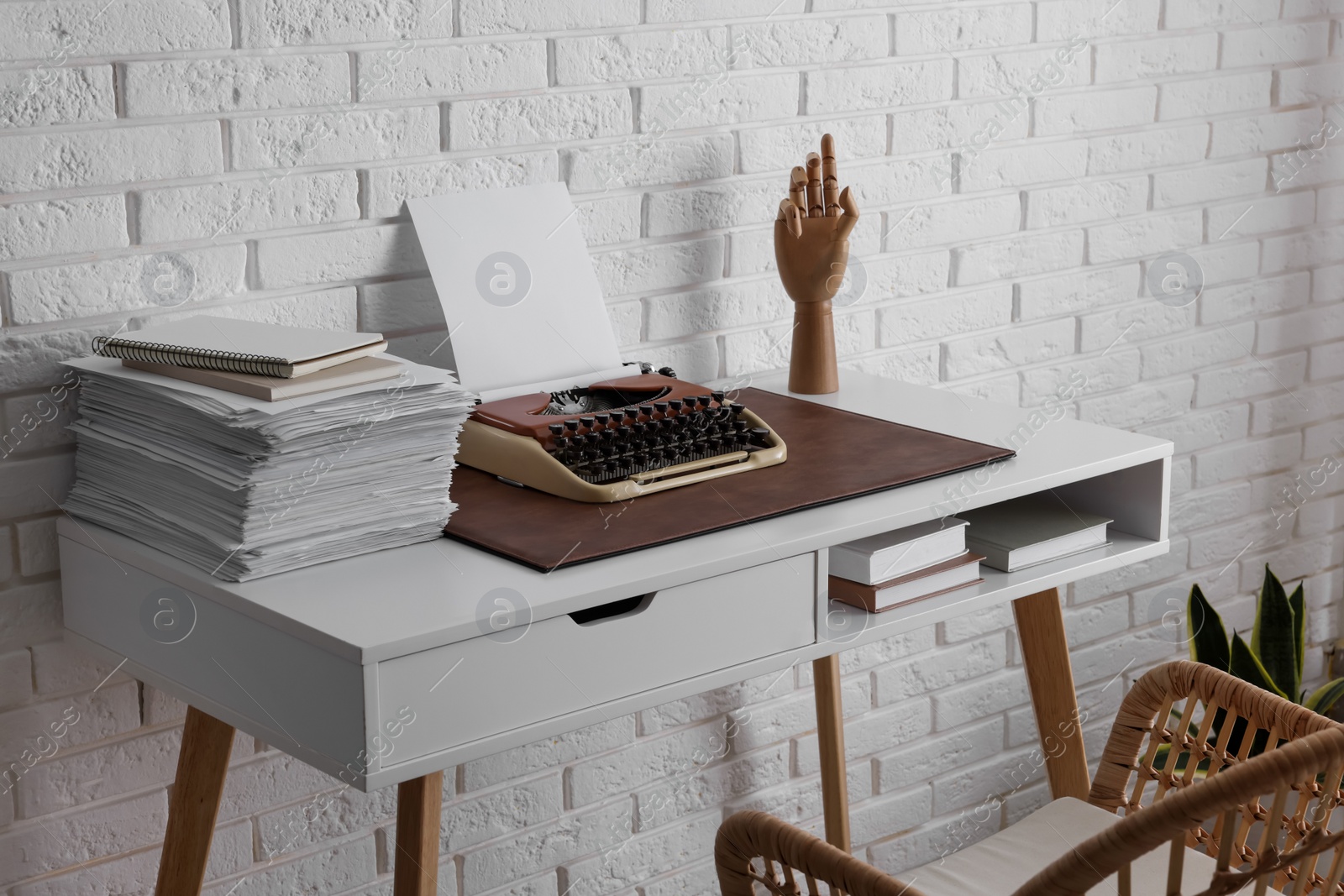 Photo of Comfortable writer's workplace with typewriter on desk near white brick wall