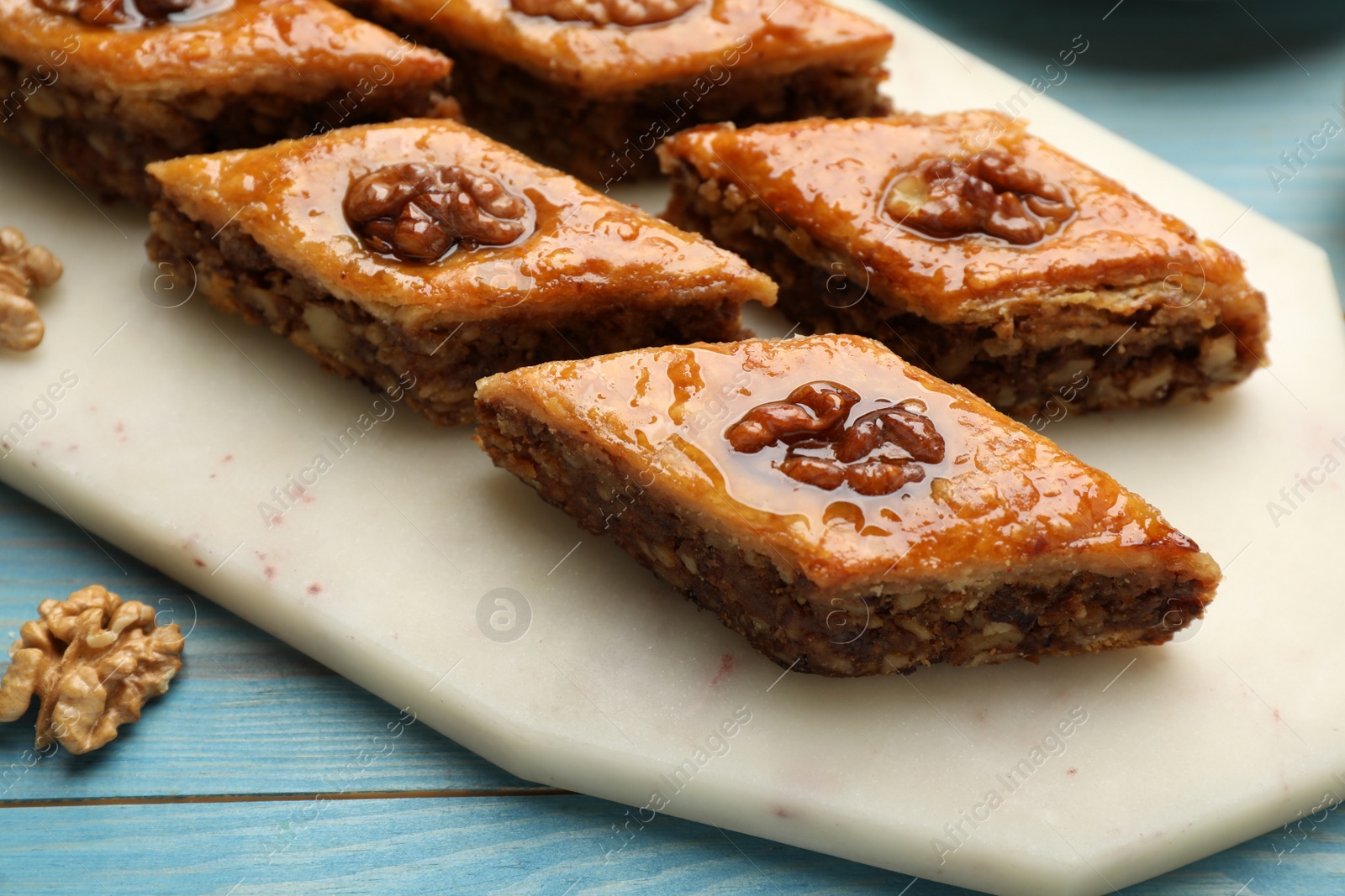 Photo of Delicious sweet baklava with walnuts on turquoise wooden table, closeup