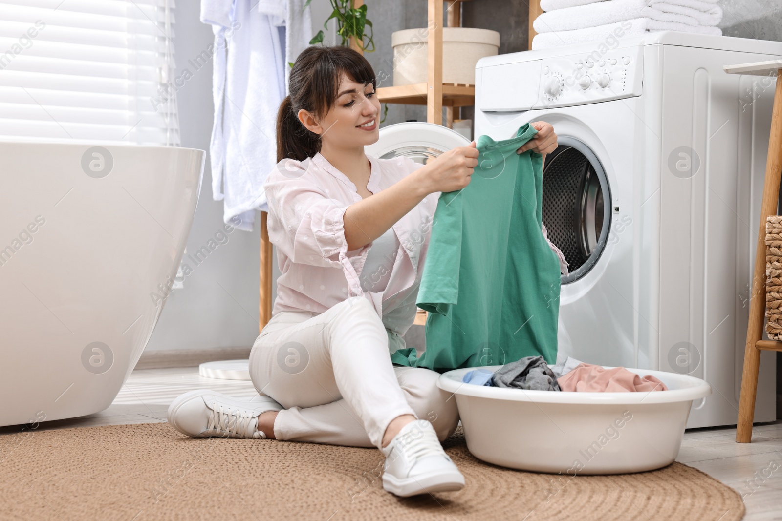 Photo of Happy young housewife with laundry near washing machine at home