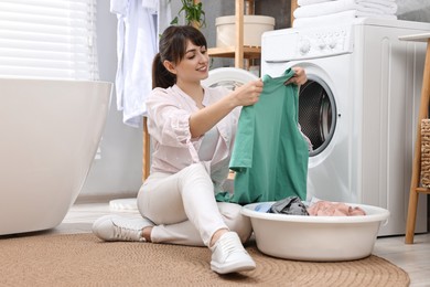 Happy young housewife with laundry near washing machine at home