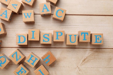 Photo of Cubes with word Dispute on light wooden table, flat lay