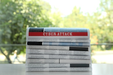 Newspapers with headline CYBER ATTACK stacked on white table outdoors
