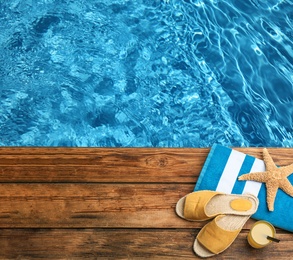 Beach accessories on wooden deck near swimming pool, flat lay. Space for text 