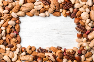 Frame made of organic mixed nuts on white wooden background, top view. Space for text