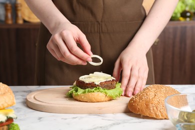 Woman making delicious vegetarian burger at white marble table, closeup