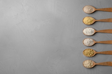 Spoons with different types of flour on gray background