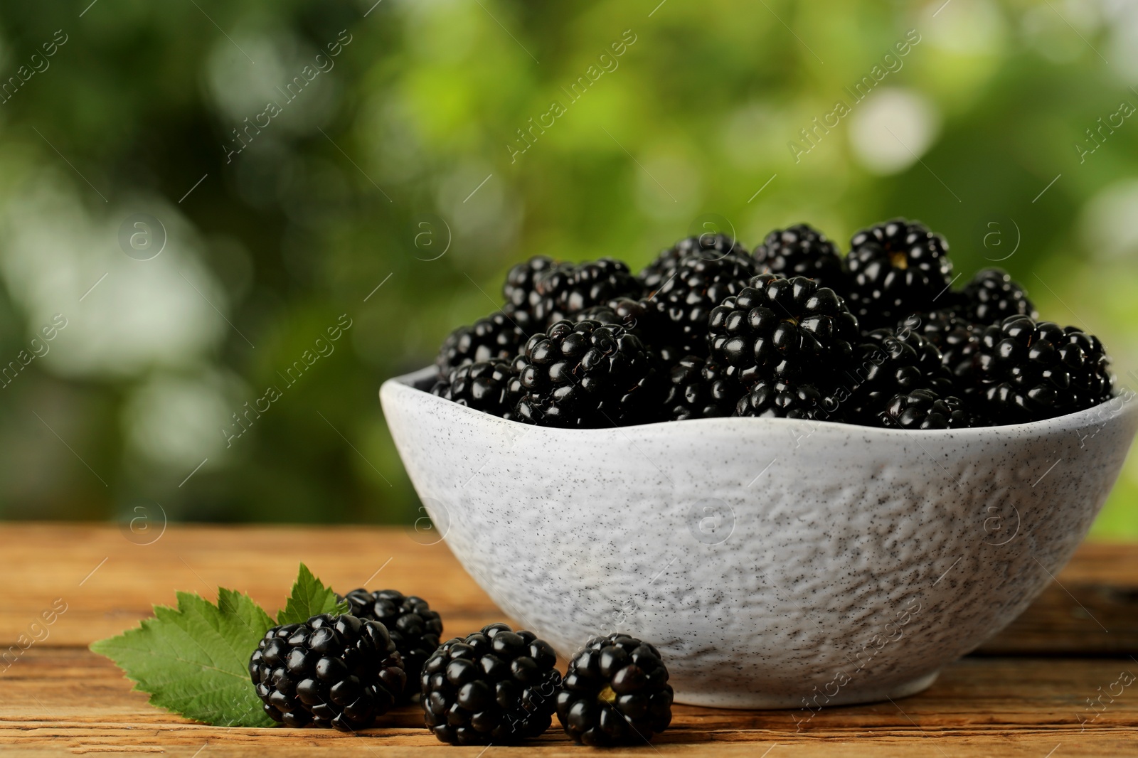 Photo of Bowl of fresh ripe blackberries on wooden table outdoors, closeup. Space for text