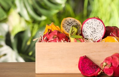 Crate with delicious cut and whole dragon fruits (pitahaya) on wooden table