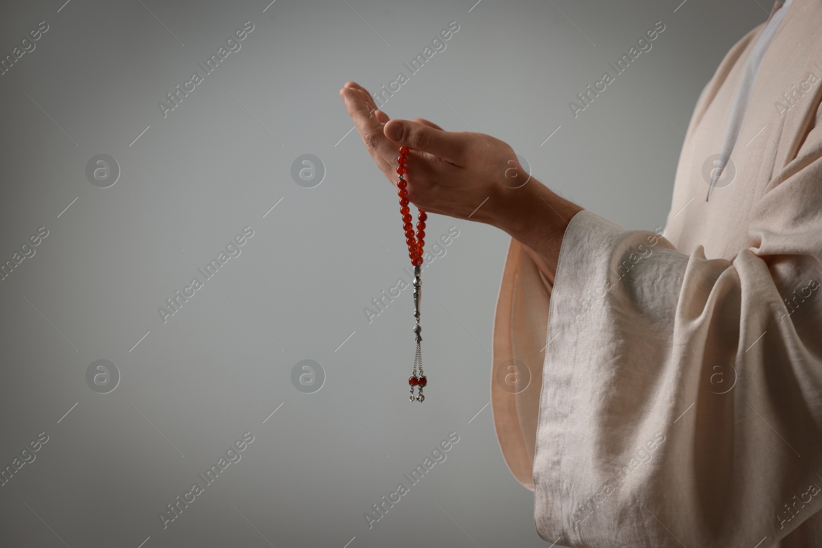 Photo of Muslim man with misbaha praying on light grey background, closeup. Space for text