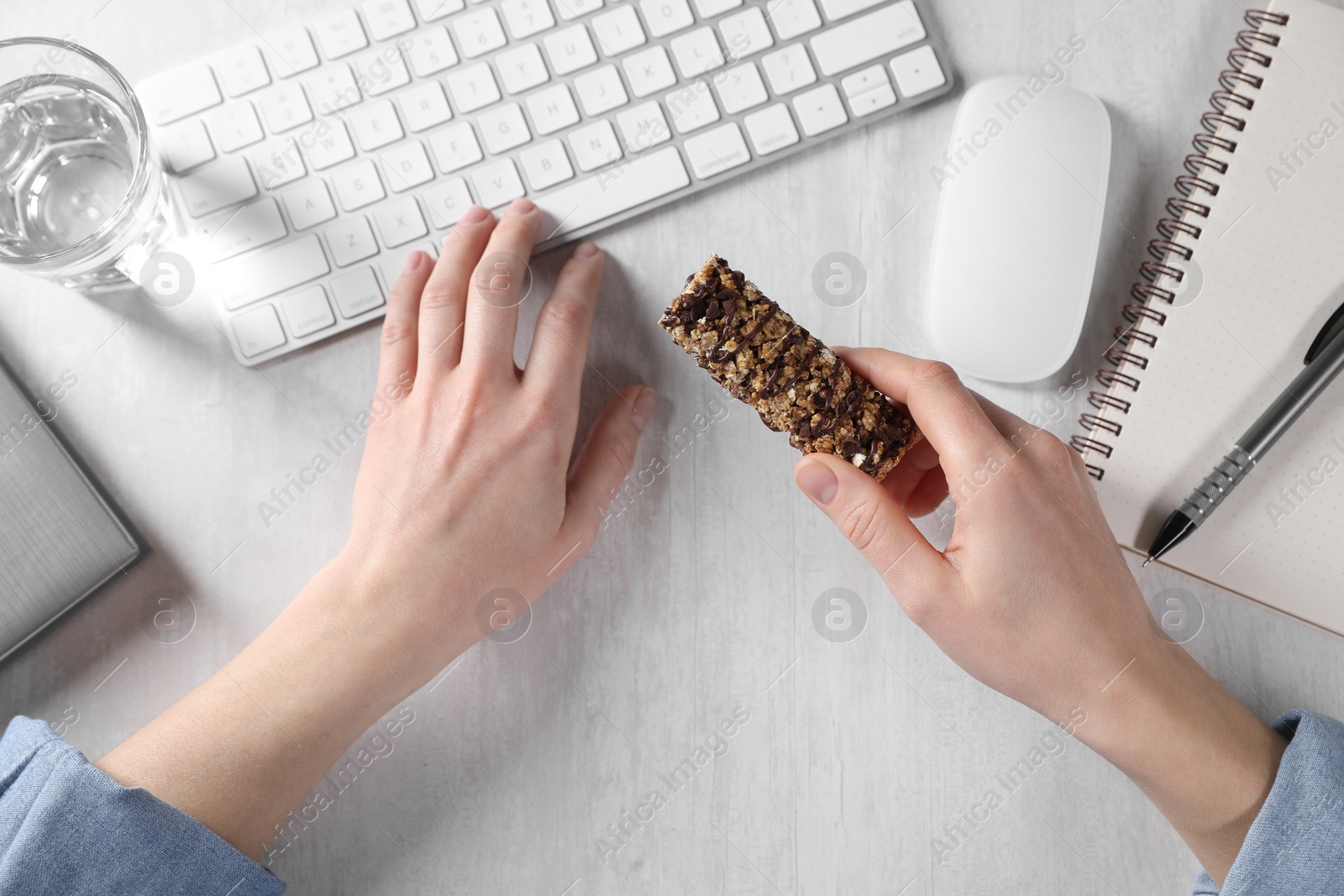 Photo of Woman holding tasty granola bar working with computer at light table, top view