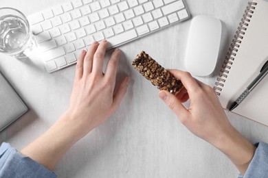 Woman holding tasty granola bar working with computer at light table, top view