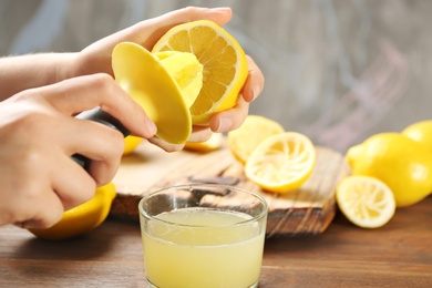 Photo of Young woman squeezing lemon juice with reamer into glass on table
