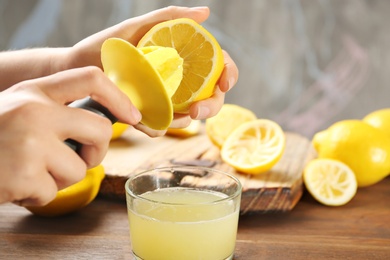 Young woman squeezing lemon juice with reamer into glass on table