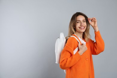 Happy woman with backpack on light grey background. Space for text