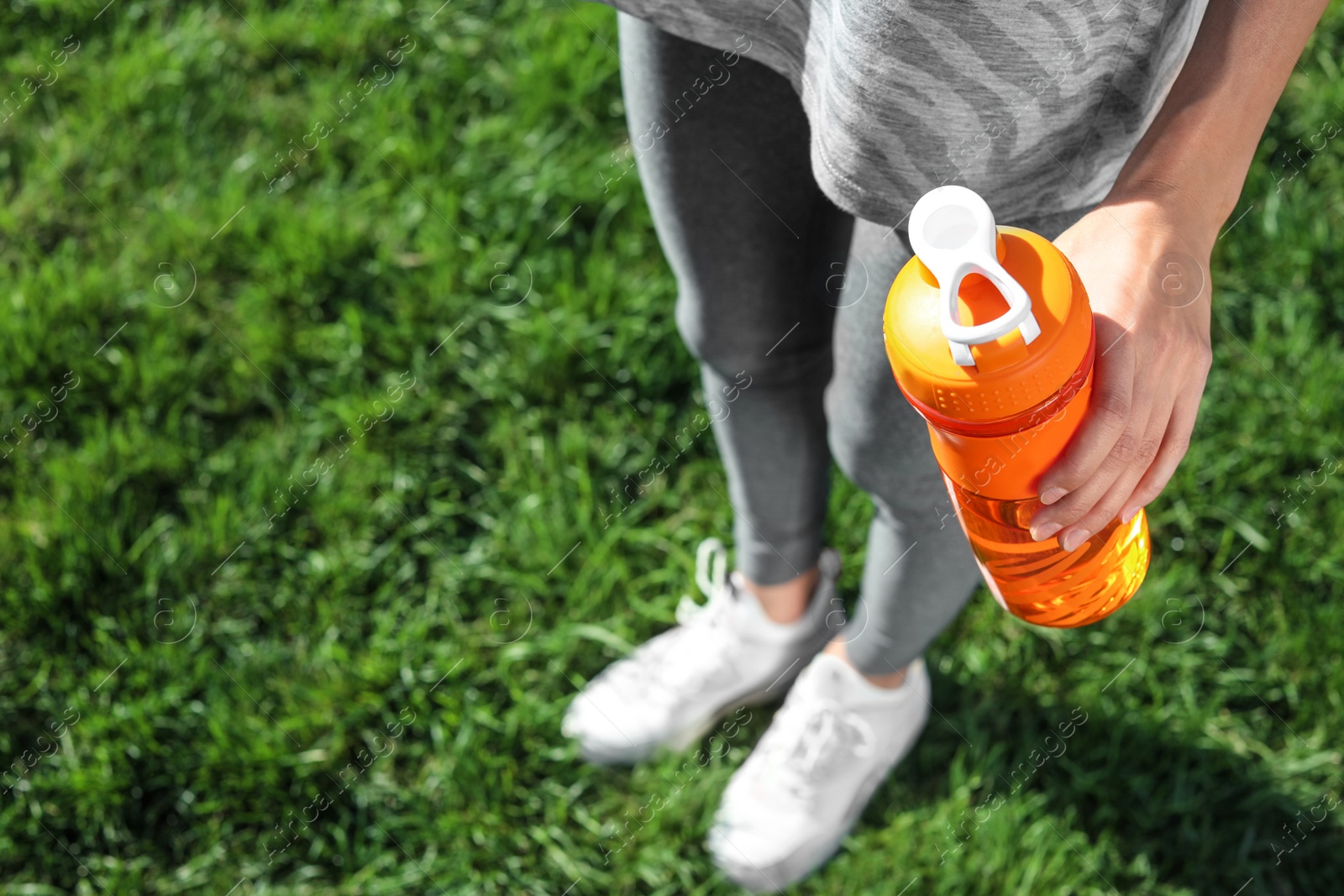 Photo of Young woman holding bottle with clean water outdoors. Space for text