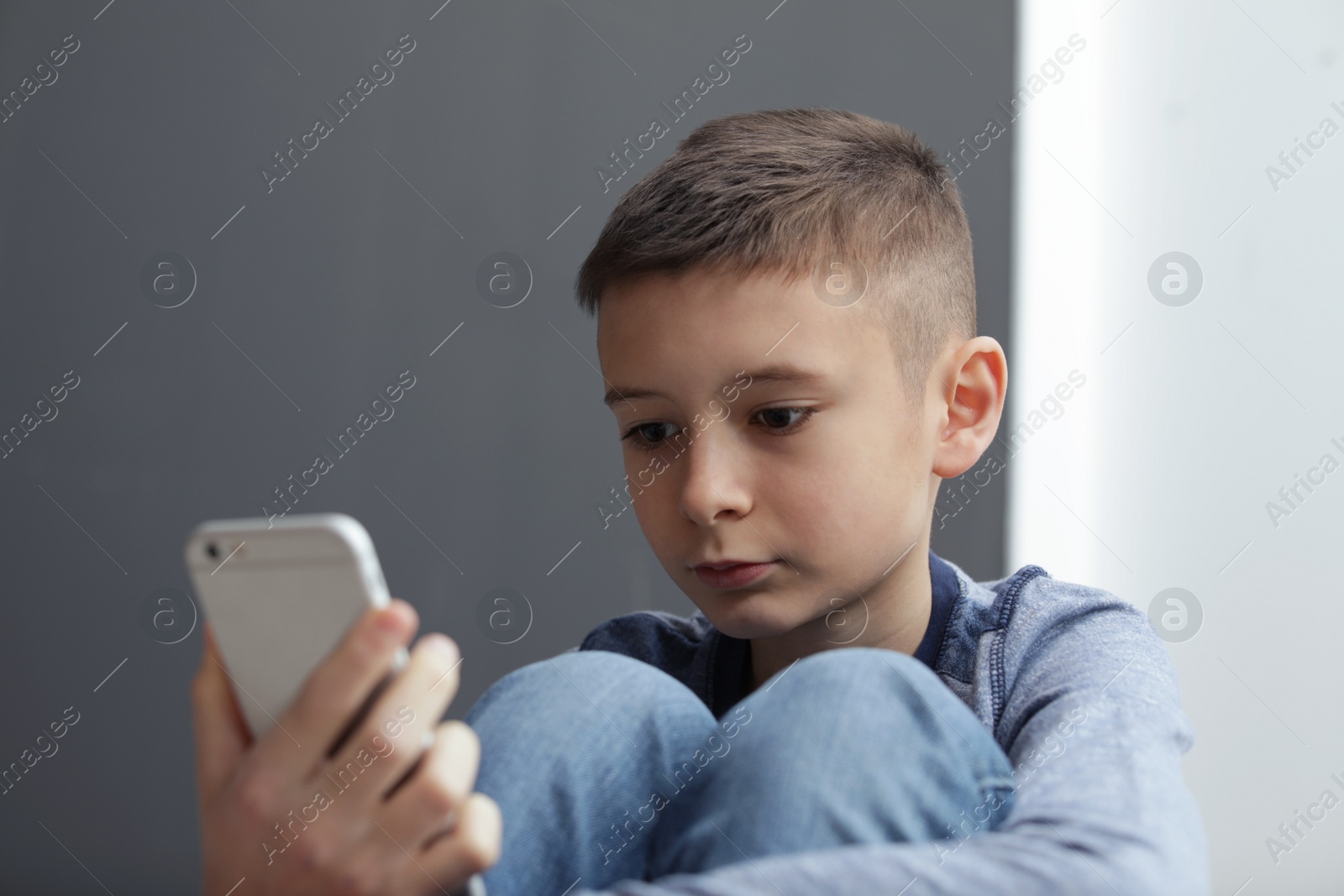 Photo of Upset preteen boy with smartphone sitting indoors