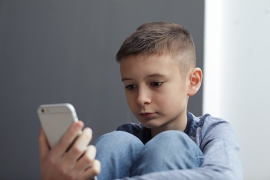Upset preteen boy with smartphone sitting indoors