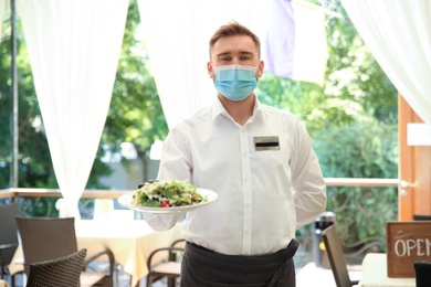 Photo of Waiter with plate of salad in restaurant. Catering during coronavirus quarantine
