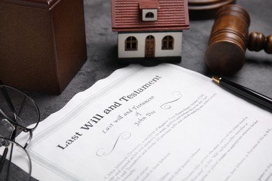 Photo of Last will and testament near house model, glasses and gavel on grey table, closeup