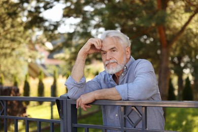 Photo of Portrait of serious senior neighbour leaning on fence outdoors