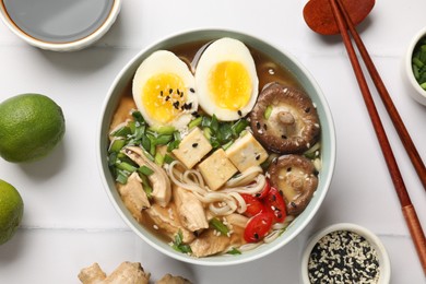 Photo of Noodle soup. Bowl of delicious ramen, ingredients and chopsticks on white tiled table, flat lay