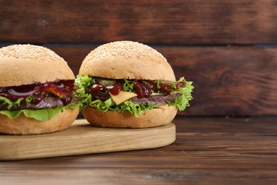 Photo of Board with delicious cheeseburgers on wooden table, closeup. Space for text