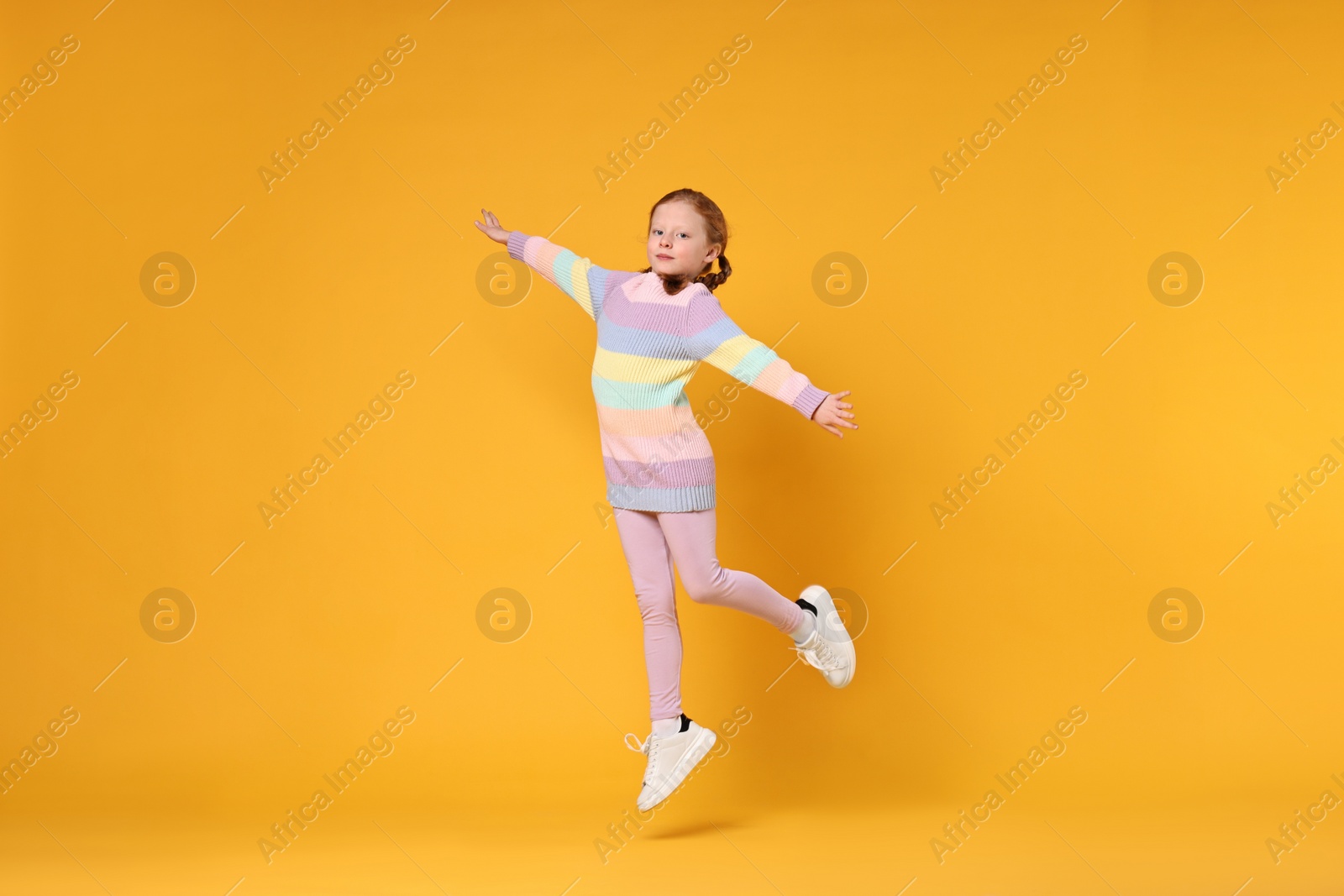 Photo of Cute little girl dancing on orange background