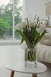 Photo of Beautiful bouquet of willow branches and tulips in vase on table indoors
