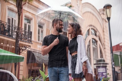 Young couple with umbrella enjoying time together under rain on city street