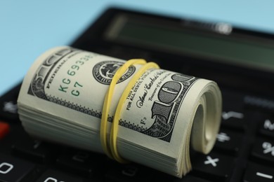 Money exchange. Dollar banknotes and calculator on light blue background, closeup