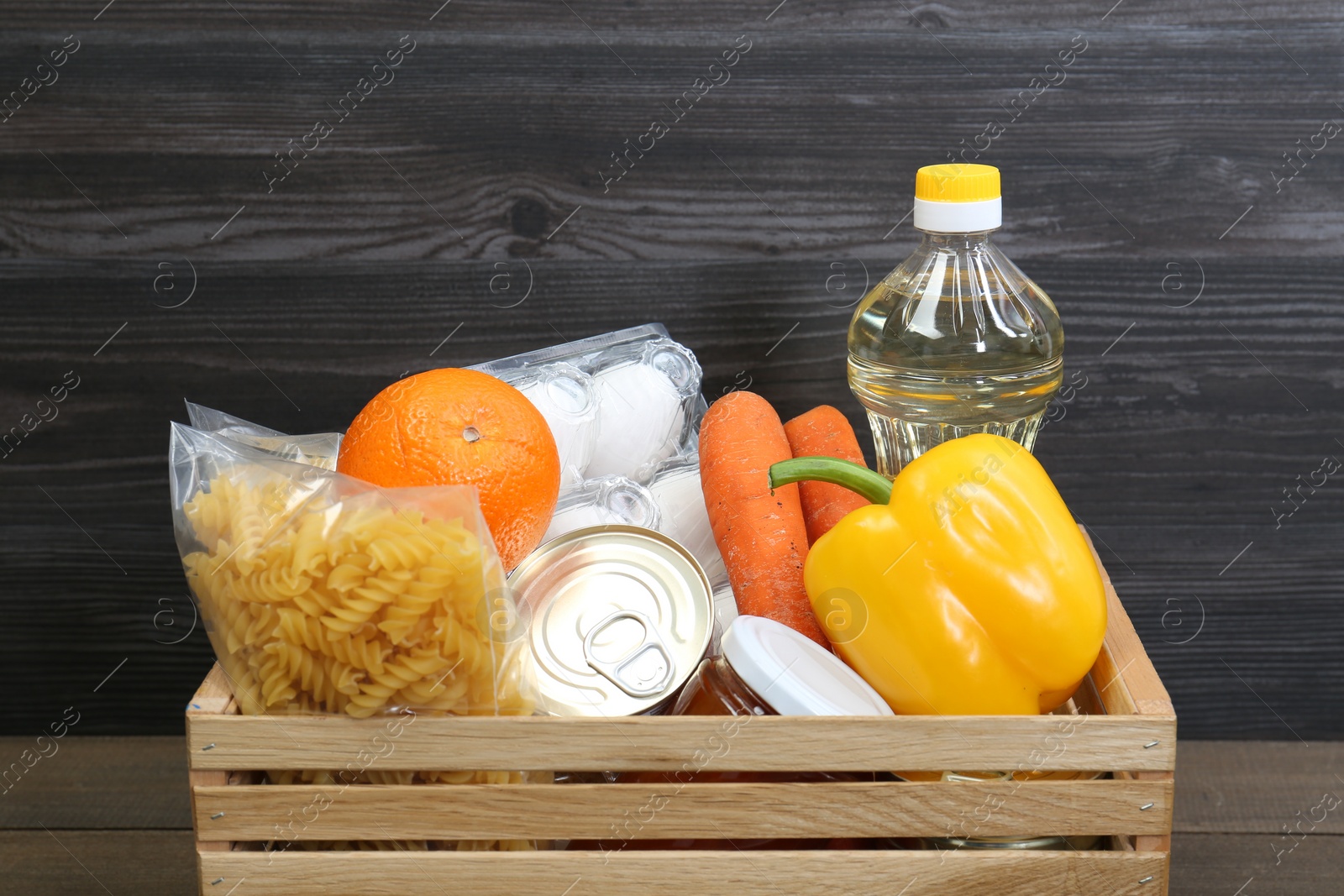 Photo of Crate with donation food against wooden background, closeup