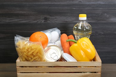 Crate with donation food against wooden background, closeup