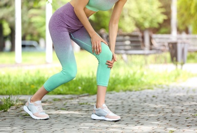 Young woman suffering from knee pain in park, closeup