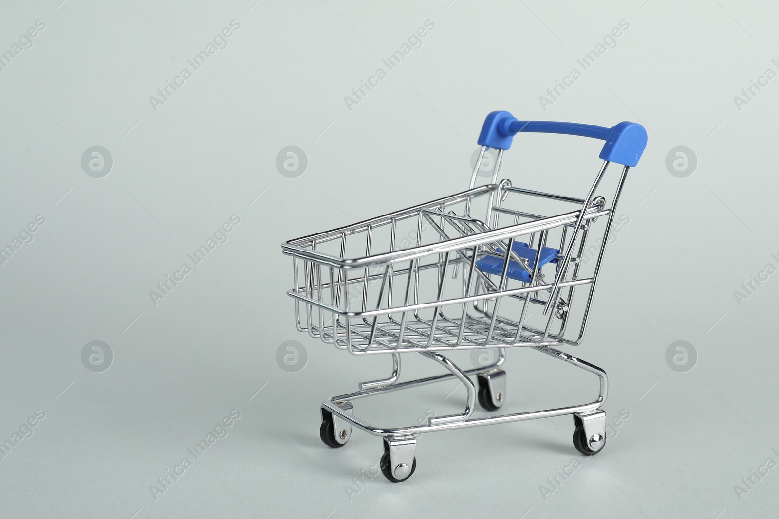 Photo of Small metal shopping cart on light background, space for text