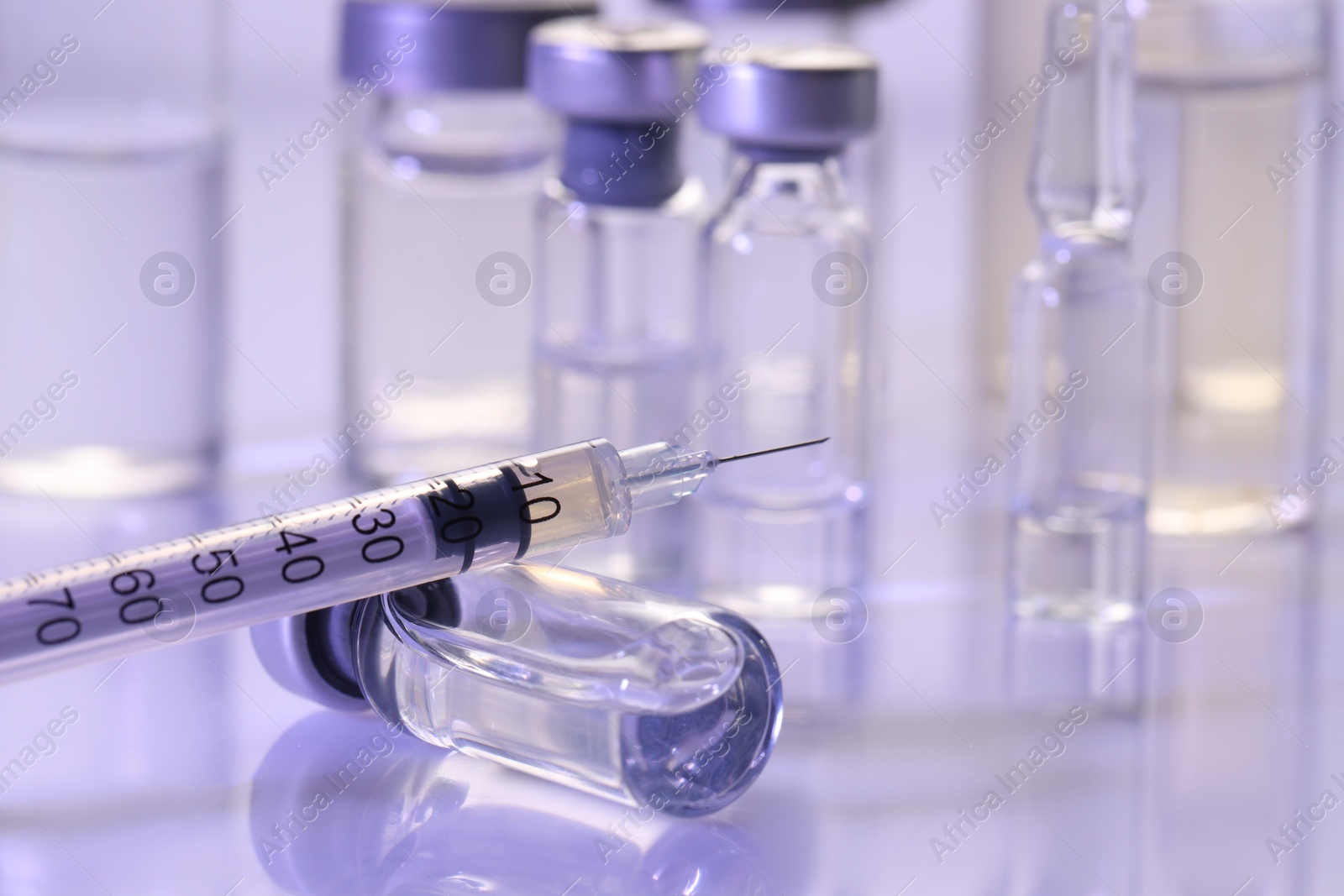 Photo of Glass vial and syringe with medication on white table, closeup. Space for text