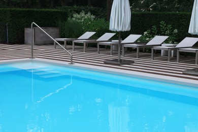 Photo of Many sunbeds and umbrellas near outdoor swimming pool