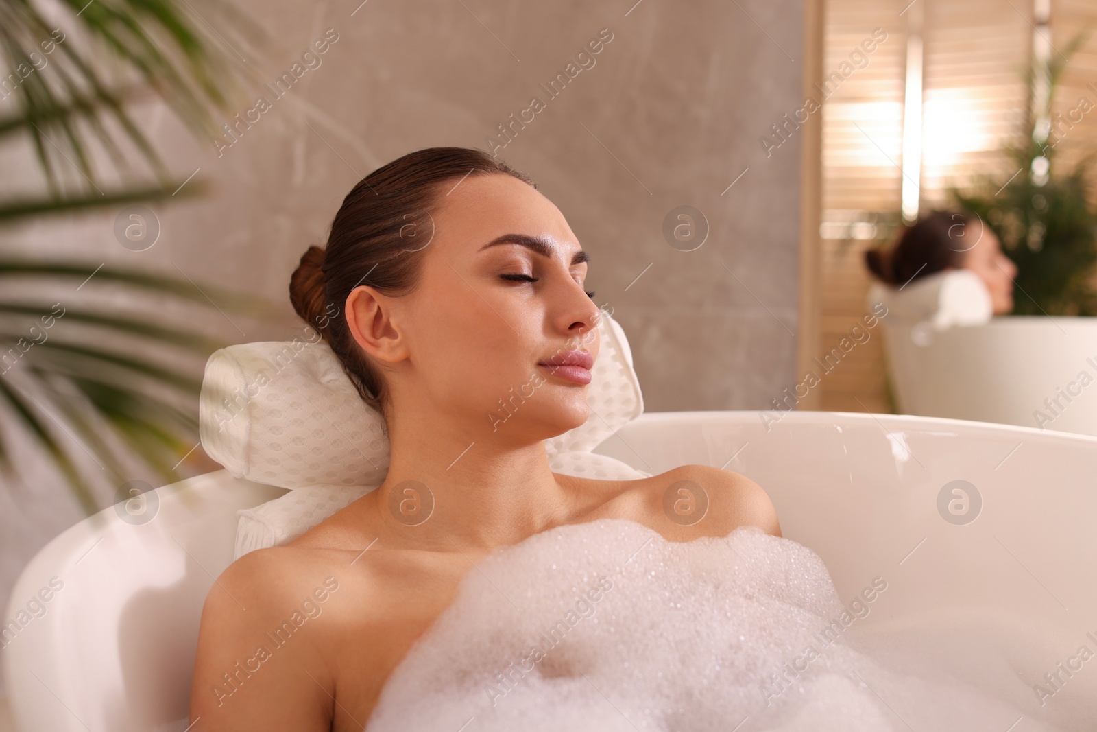 Photo of Young woman using pillow while enjoying bubble bath indoors